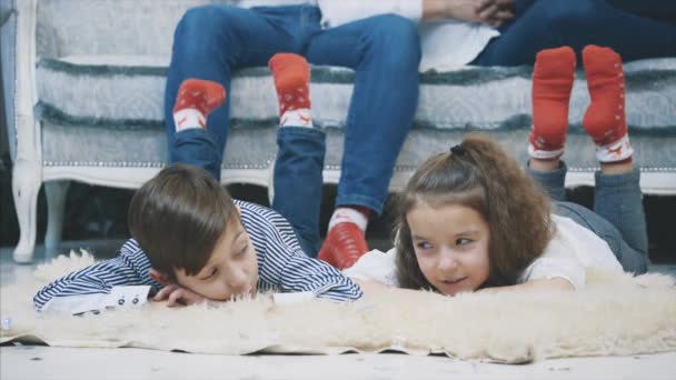 Hermano pequeño y hermana hablando encantadora, compartiendo historias, mientras yacía en la alfombra de piel caliente . — Vídeos de Stock