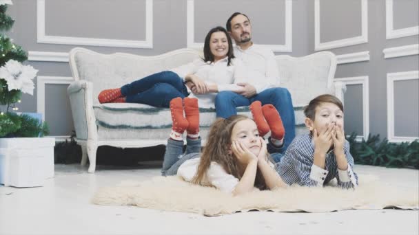 Los miembros encantadores de la familia en calcetines rojos se reúnen año nuevo. Niños soñolientos están tendidos en la alfombra blanca . — Vídeos de Stock