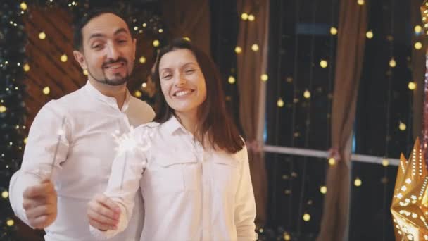 Couple singing Christmas carols at on Christmas Eve, holiding bengal lights and looking completely delighted. — Stok video