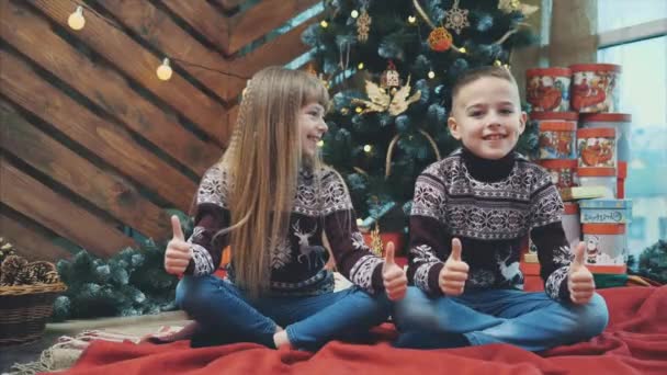 Bělošští sourozenci v bílých vlněných svetrech ukazují palce nahoru, spokojení s atmosférou nového roku. — Stock video