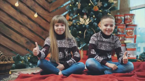 Białe rodzeństwo noszone w wełnianych swetrach ma kciuki w górze, zadowolone z noworocznej atmosfery.. — Wideo stockowe