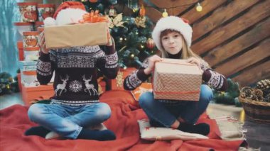 Ren geyiği desenli Noel süveterli kardeşler, dalga geçmeler, hediye kutularıyla oynamalar..