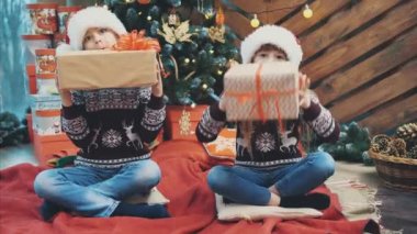 Ren geyiği desenli Noel süveterli kardeşler, dalga geçmeler, hediye kutularıyla oynamalar..