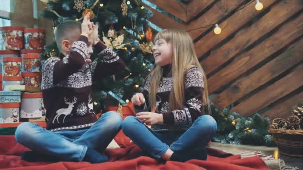 Grimacing niños en suéteres de lana muestran grandes orejas con las manos y poner las lenguas en el fondo de madera con árbol de Navidad . — Vídeos de Stock