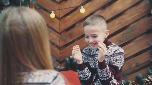 4k wideo chłopca i dziewczyny grających klaskanie gry, zabawy razem, na drewnianym tle Bożego Narodzenia. Dziewczyna siedząca tyłem do kamery na czole zamazana. — Wideo stockowe