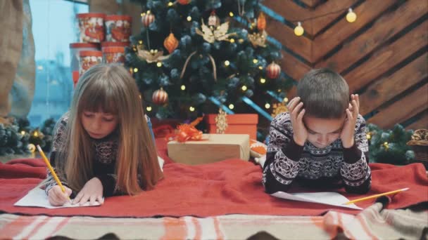 集中した子供たちは、すべての願いと欲望を考え、サンタに手紙を書くプロセスに関与しています. — ストック動画