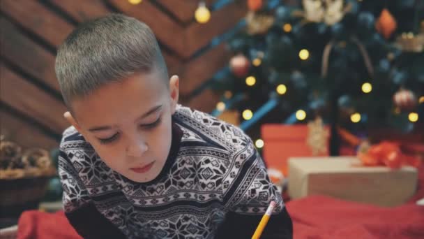 小男孩的衣服，确信他全年都表现得很好，正在给圣诞老人写信以得到礼物. — 图库视频影像