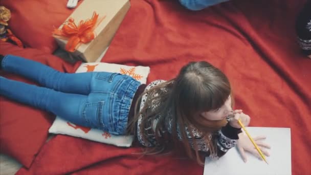 Vista dall'alto della ragazza bionda che pensa a cosa scrivere nella lettera al Polo Nord, sdraiata su una coperta rossa la sera d'inverno . — Video Stock