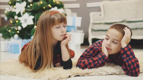 Cute little kids spend pleasant time together, communicating on the carpet near Christmas tree. — Stock Video