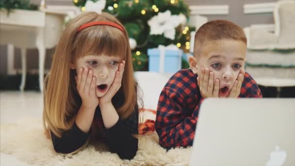 4k video van mooie broers en zussen kijken naar een horror film tijdens het leggen onder Kerstmis spar op nieuwjaar ochtend. — Stockvideo