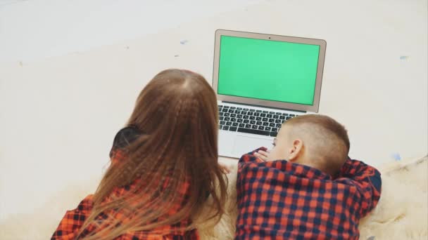 Küçük çocuklar, krom anahtar yeşil ekranlı dizüstü bilgisayar ekranına bakıyor, tatil akşamında beyaz halıda yatıyor.. — Stok video