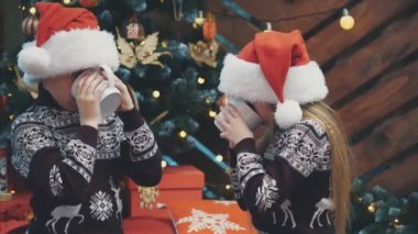 Noel Baba şapkalı ve yün kazaklı güzel çocuklar, Noel ağacının yanında oturuyorlar, ellerinde kakao bardakları, keyifli ve memnun görünüyorlar..
