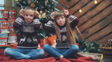 Yünlü süveter giyen suratsız çocuklar büyük kulakları elleriyle gösterir ve tahta arka plana Noel ağacı ile dillerini koyarlar..