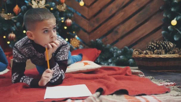 4k video de niño reflexivo en busca de algo para escribir en una carta a santa, pero él no tiene idea . — Vídeos de Stock