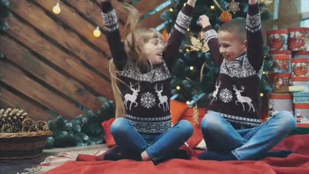 Vídeo perfecto de timelpase donde niño y niña se ríen, levantando las manos como ganadores y divirtiéndose juntos cerca del árbol de Navidad . — Vídeo de stock