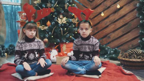 Fénykép rénszarvas agancsot viselő gondolkodású gyerekekről Szenteste, azon tűnődve, mit kapnak ajándékba.. — Stock videók