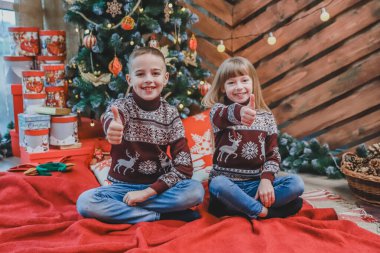 Bordo yünlü süveter giyen beyaz kardeşler yeni yıl atmosferinden memnunlar ve başparmaklarını gösteriyorlar..
