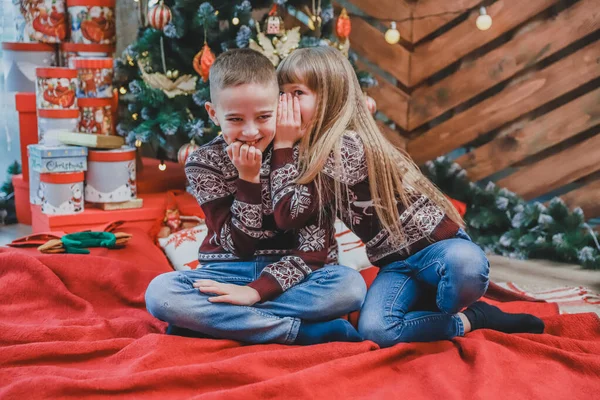 家で赤い毛布の上に座っている彼女の兄に耳を傾け、クリスマスを祝う女の子の甘いショット. — ストック写真
