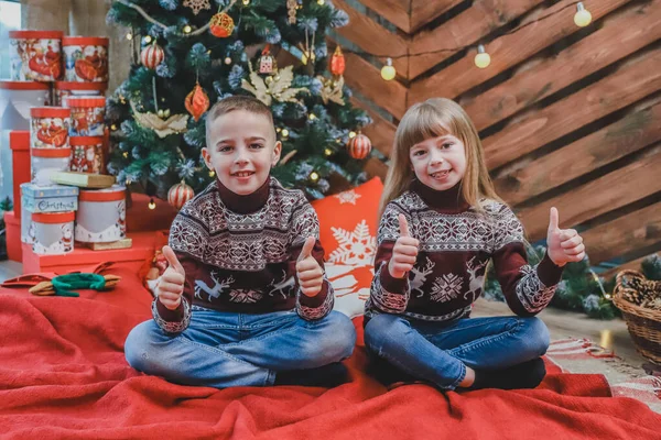 Irmãos caucasianos vestidas em blusas de lã clarete estão mostrando polegares para cima, satisfeito com a atmosfera do ano novo . — Fotografia de Stock