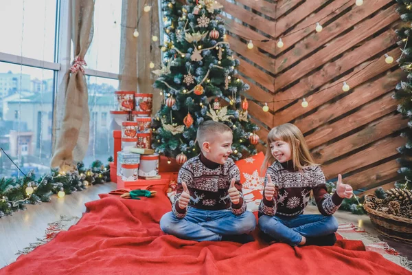 Irmãos caucasianos vestidas em blusas de lã clarete estão mostrando polegares para cima, satisfeito com a atmosfera do ano novo . — Fotografia de Stock