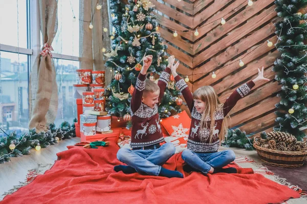 小さな男の子と女の子が笑っていて、勝者のように手を上げて、クリスマスツリーの近くで一緒に楽しんでいる完璧なイメージ. — ストック写真