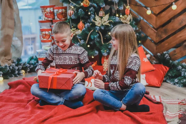 Dos niños compartiendo cajas de regalo de Navidad sentados en un ambiente diseñado para Navidad . — Foto de Stock