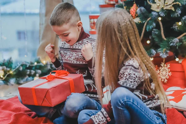 Dos niños compartiendo cajas de regalo de Navidad sentados en un ambiente diseñado para Navidad . — Foto de Stock
