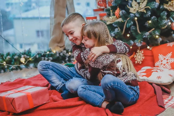 Immagine di fratello e sorella in cappelli di Babbo Natale, teneramente abbracciati, che condividono regali di Natale su sfondo di legno . — Foto Stock