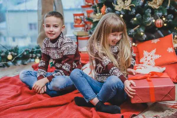 Dos niños compartiendo cajas de regalo de Navidad sentados en un ambiente diseñado para Navidad . — Foto de Stock