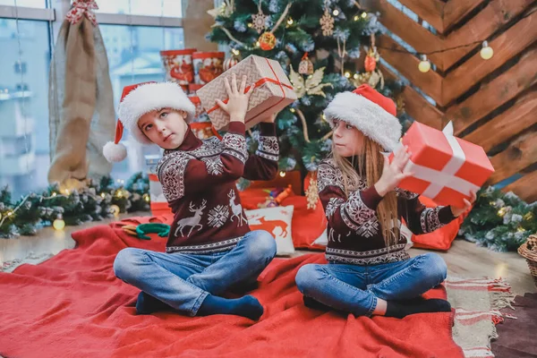 Foto de cuerpo completo de niños lindos sentados en posición lotos con regalos de Navidad, averiguar lo que hay dentro . — Foto de Stock