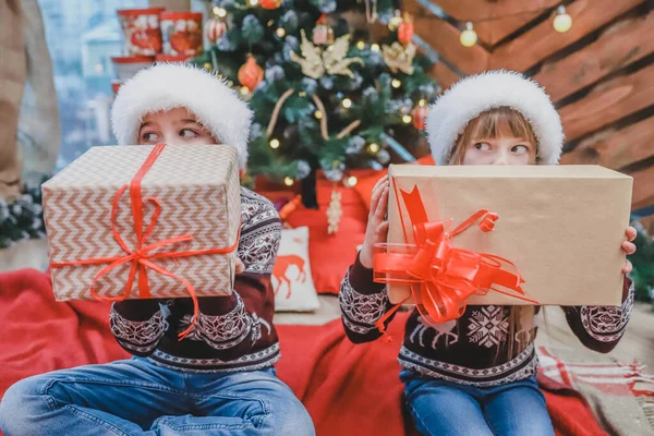 Photo rapprochée de fils et de fille qui ont préparé des cadeaux de Noël pour leurs parents et les montrent à la caméra, fière de ce qu'ils ont fait . — Photo