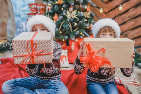 Foto de cerca del hijo y la hija que prepararon regalos de Navidad para sus padres y los están mostrando a la cámara, luciendo orgullosos de lo que han hecho . — Foto de Stock