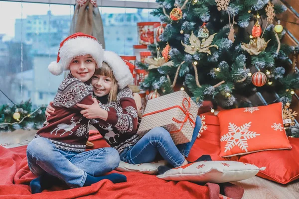Dwoje dzieci w kapeluszach Santa dzieląc pudełka świąteczne prezent siedzi w świątecznej atmosferze zaprojektowane. — Zdjęcie stockowe