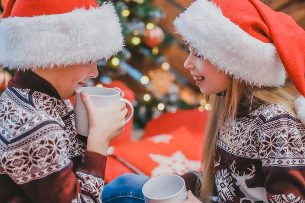 Καλλιεργημένη φωτογραφία του αστείου αδελφού και της αδελφής πίνοντας ζεστή σοκολάτα και κάνοντας πλάκα σε ένα άνετο σαλόνι την παραμονή των Χριστουγέννων. — Φωτογραφία Αρχείου