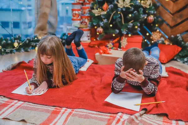 Pequenos irmãos loiros têm certeza de que eles se comportaram bem o ano inteiro e agora eles estão escrevendo carta para o Papai Noel para obter o presente . — Fotografia de Stock