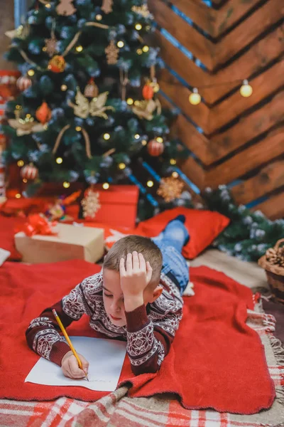 Menino, certo de que ele se comportou bem o ano inteiro, está escrevendo uma carta para o Papai Noel para obter o presente . — Fotografia de Stock