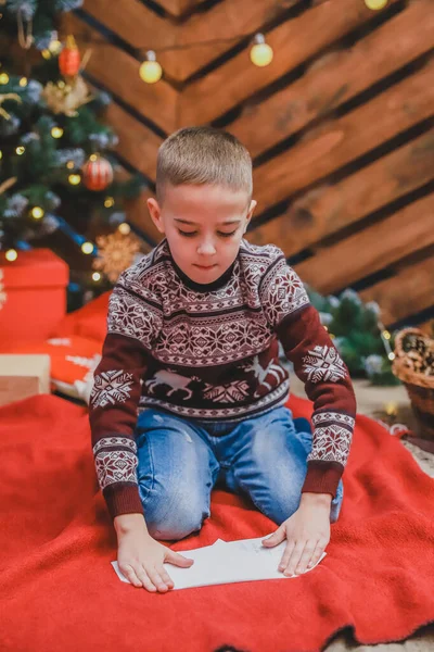 Niño feliz en suéter de reno de punto, sellando sobre a Santa con regalos de Navidad lista de deseos . — Foto de Stock