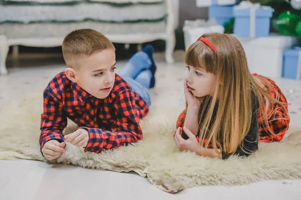 Lächelnder Bruder und kleine Schwester liegen in rot karierten Kleidern auf dem Wollteppich. — Stockfoto