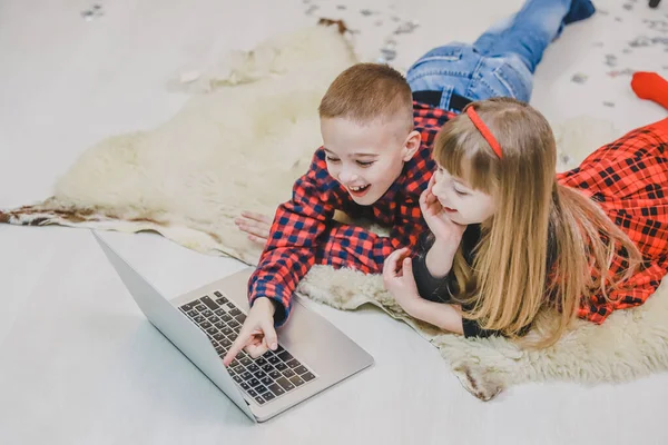 Radosne dzieci grają w nowoczesne ciekawe gry na laptopie w pokoju urządzonym na Nowy Rok. — Zdjęcie stockowe