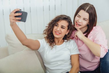 Kanepede oturan, selfie çeken, poz veren, surat yapan sevimli genç kızlar. Esmer kız dilini gösteriyor..
