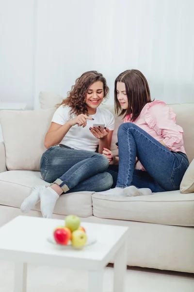 Dos compañeros de cuarto usando sus teléfonos inteligentes en casa sentados en un sofá en la sala de estar . — Foto de Stock