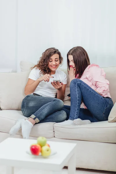 Dos compañeros de cuarto usando sus teléfonos inteligentes en casa sentados en un sofá en la sala de estar . — Foto de Stock