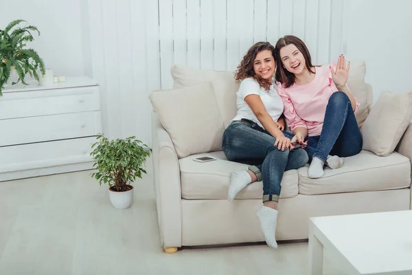 Dvě úžasné dívky sedící na gauči, objímající se a usmívající se do kamery. — Stock fotografie