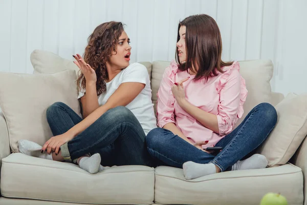 Dos amigas atractivas sentadas en el sofá en posición lotos, con teléfonos inteligentes en las manos, discutiendo, teniendo conflicto . —  Fotos de Stock