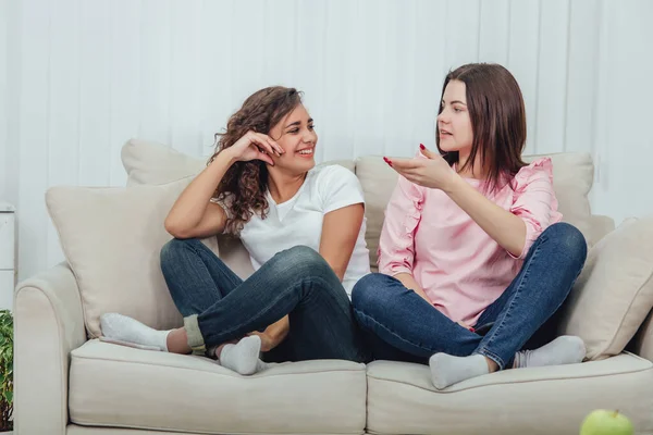 Dos amigas atractivas sentadas en el sofá en posición lotos, hablando con entusiasmo . —  Fotos de Stock