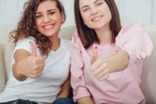 Kanepede yan yana oturan bulanık tatlı kızlar başparmaklarını kaldırıyor, güzel gülümsüyor. Öndeki başparmaklara odaklan..