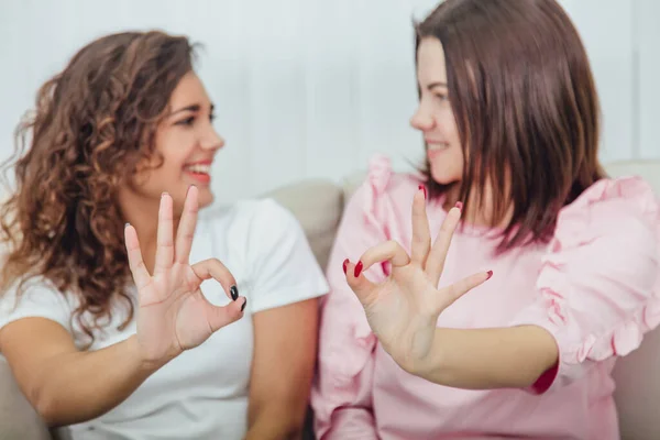 Amigos adoráveis borrados em roupas casuais sentados lado a lado, mostrando sinal ok, olhando um para o outro, sorrindo . — Fotografia de Stock