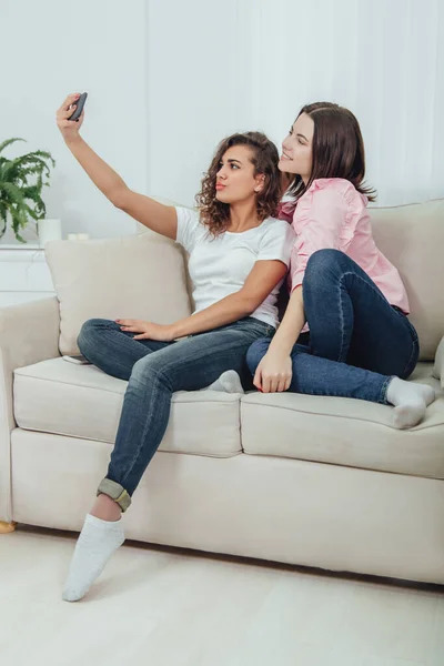 Carino giovani ragazze sedute sul divano, prendendo selfie, posa, fare facce . — Foto Stock