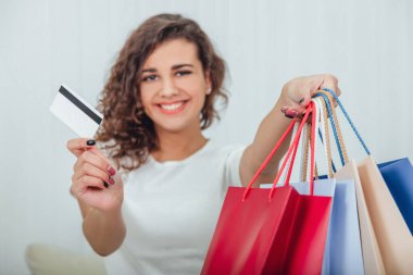 Bulanık, neşeli, pırıl pırıl gülüşlü kız bir elinde dört renkli alışveriş çantası, diğerinde de kameraya kredi kartı uzatıyor..