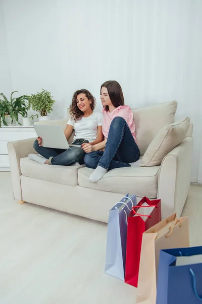 Two happy female friends sitting on the sofa, at home, using laptop for shopping online. — Stock Photo, Image